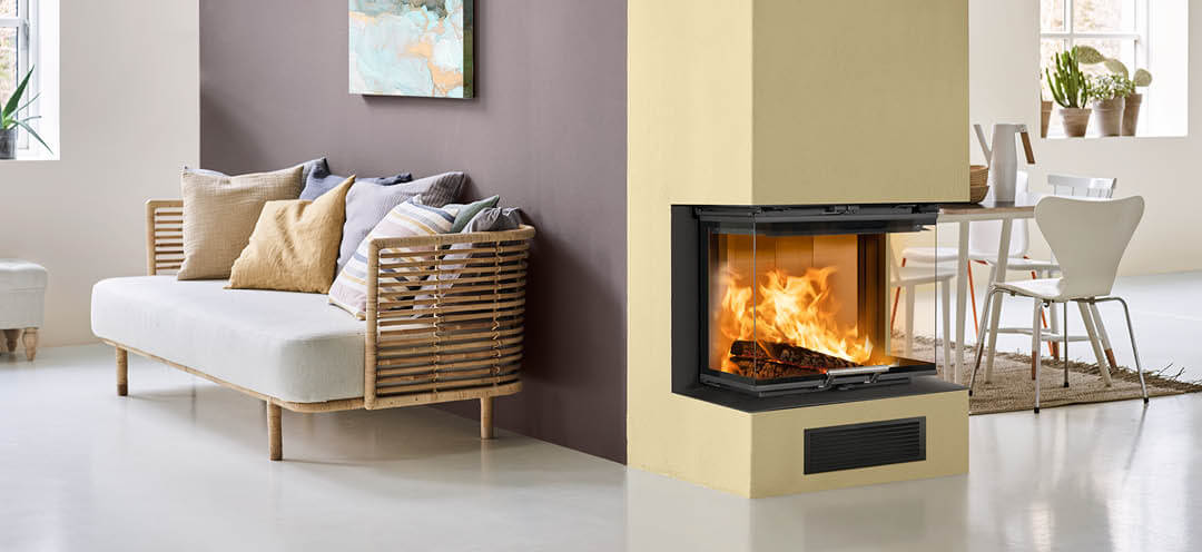 En pejs malet gul i et hvidt rum med køkken på den ene side og sofa på den anden