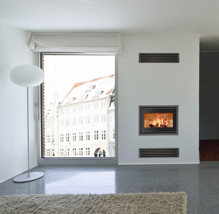 Sort pejseindsats med flammer Scan 1005 indbygget i væg i hvid stue med store vinduespartier