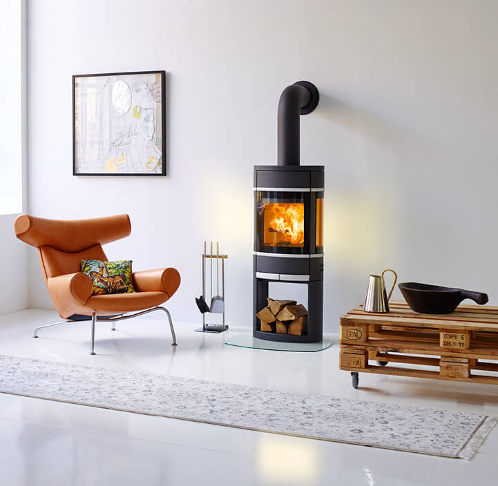 Sort pejs Scan 68 brænder i et hvidt rum med en cognacfarvet stol og et pallebord ved siden af